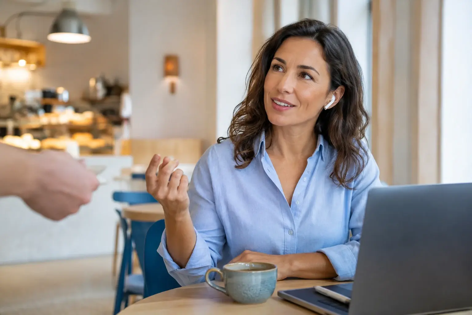 Escena ilustrativa de una mujer hablando en una cafetería, con un portátil y un café.